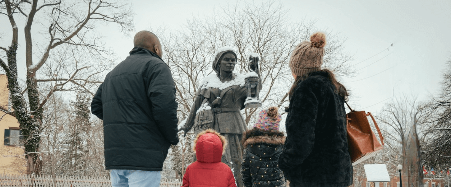 Family in standing in front of the Harriet 塔布曼 Bronze Statue in the courtyard of the Equal Rights Heritage Center in the winter with snow in the ground
